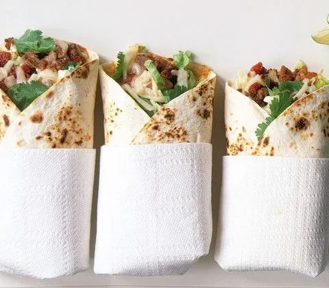 Martha Stewart beef-and-potato burritos wrapped in paper napkins with cilantro, lettuce and lime wedges