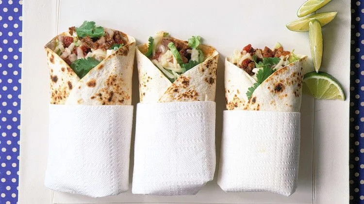 Martha Stewart beef-and-potato burritos wrapped in paper napkins with cilantro, lettuce and lime wedges