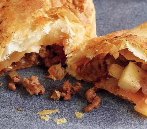Martha Stewart beef and potato hand pies with golden puff pastry, one broken open to show the ground beef, potato and raisin filling