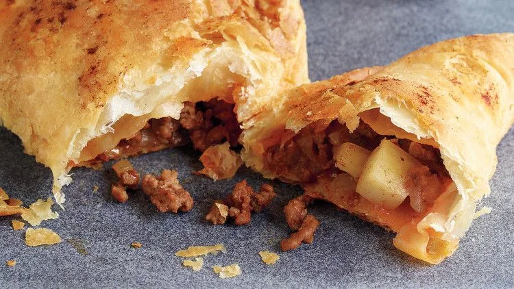 Martha Stewart beef and potato hand pies with golden puff pastry, one broken open to show the ground beef, potato and raisin filling