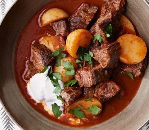 Martha Stewart beef goulash with potatoes in a paprika-red broth topped with sour cream and chopped parsley in a bowl