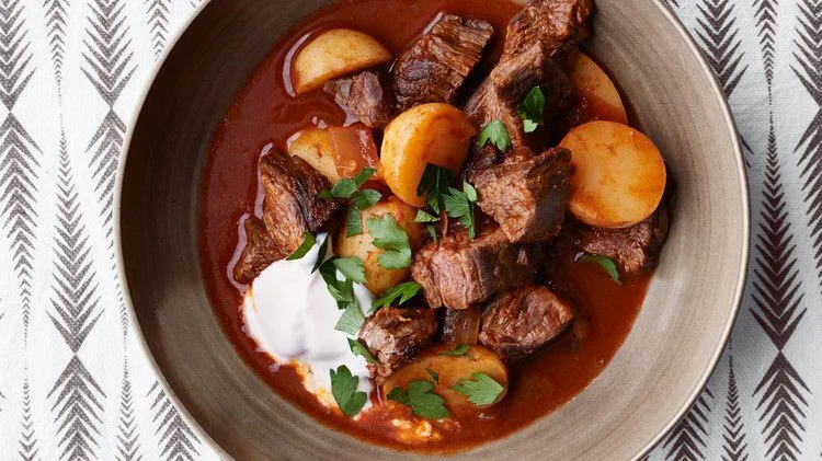 Martha Stewart beef goulash with potatoes in a paprika-red broth topped with sour cream and chopped parsley in a bowl