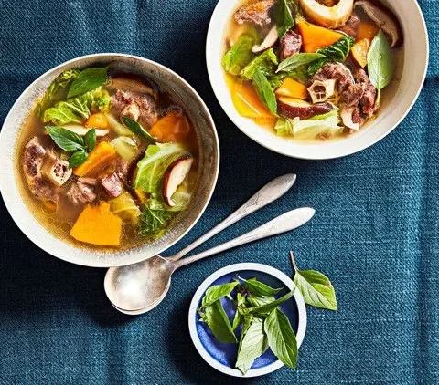 Martha Stewart beef, pumpkin and shiitake soup in two bowls with sliced mushrooms, orange pumpkin, cabbage and fresh basil leaves