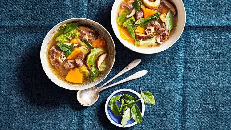 Martha Stewart beef, pumpkin and shiitake soup in two bowls with sliced mushrooms, orange pumpkin, cabbage and fresh basil leaves