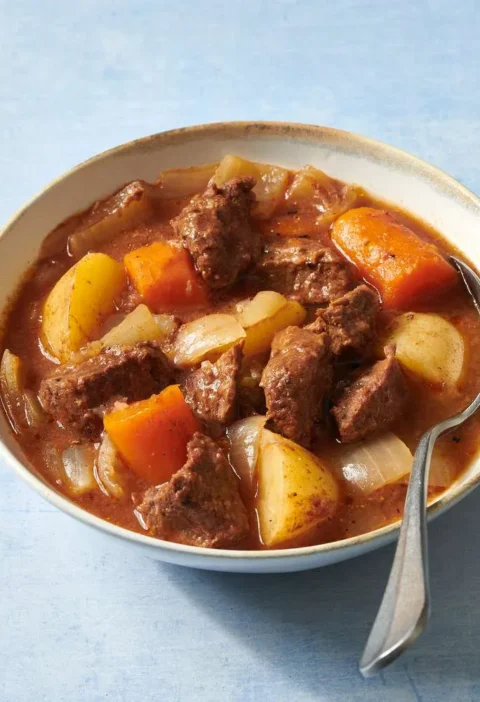 Martha Stewart beef stew with tender beef chunks, potatoes, carrots and onions in a rich tomato gravy in a white bowl with a spoon