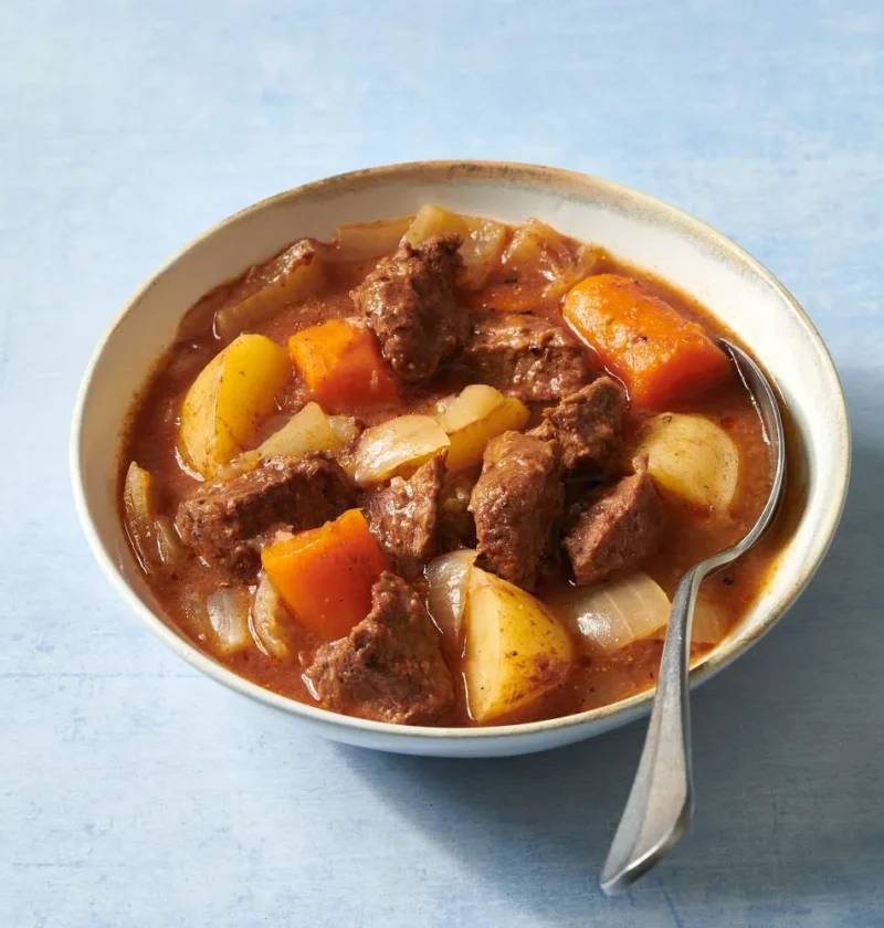 Martha Stewart beef stew with tender beef chunks, potatoes, carrots and onions in a rich tomato gravy in a white bowl with a spoon