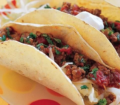 Martha Stewart beef tacos in corn tortillas filled with saucy ground beef, shredded lettuce, cilantro and sour cream on a colorful plate
