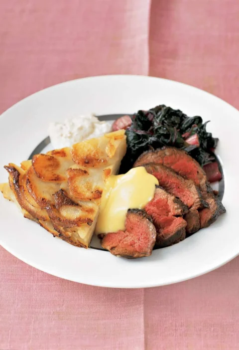 Sliced medium-rare Martha Stewart beef tenderloin served with bearnaise sauce, potato gratin and sauteed greens on a white plate