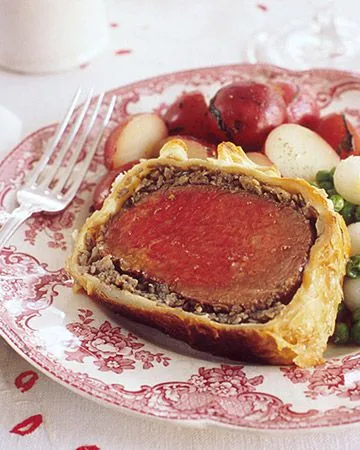 Martha Stewart beef Wellington slice with pink center and golden puff pastry served with roasted potatoes and peas