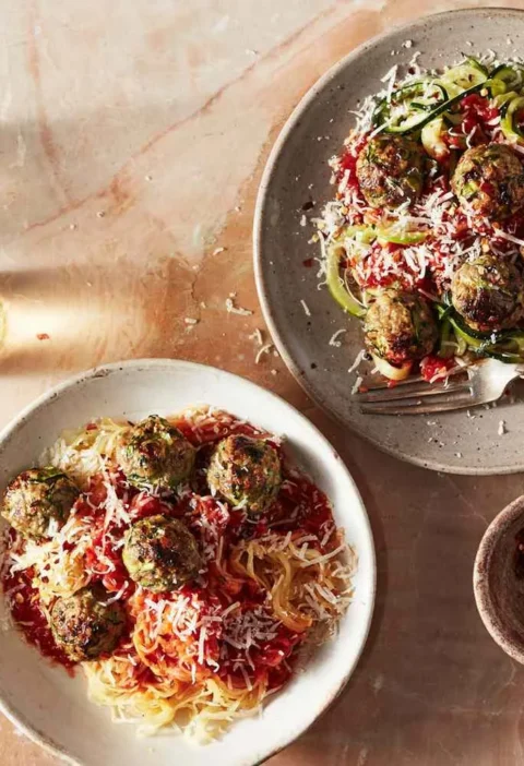 Beef-zucchini meatballs with marinara sauce and Parmesan over spaghetti squash and zucchini spirals on two plates