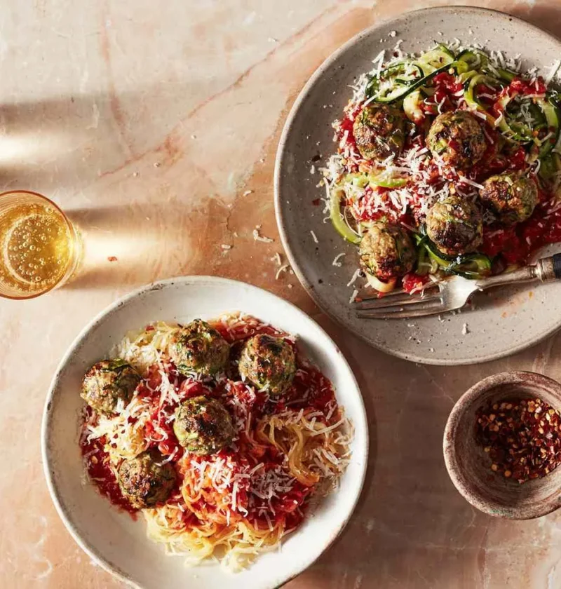 Beef-zucchini meatballs with marinara sauce and Parmesan over spaghetti squash and zucchini spirals on two plates