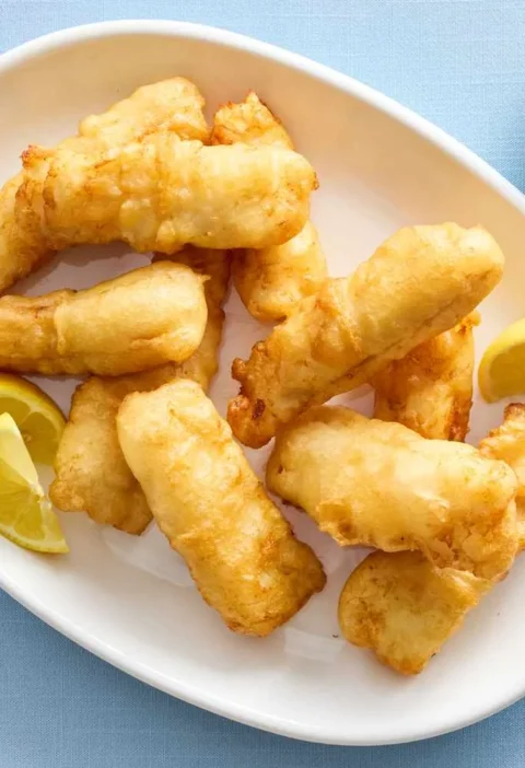 Martha Stewart beer-battered fish golden fried pieces on a white oval platter with lemon wedges and a small bowl of tartar sauce