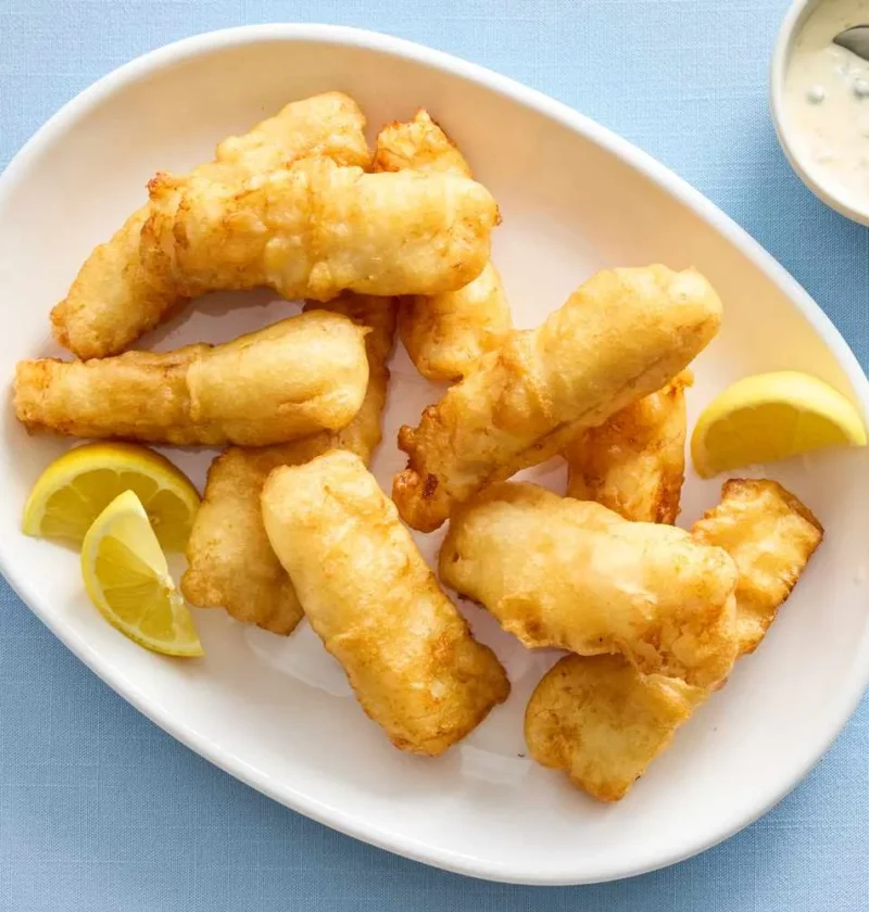 Martha Stewart beer-battered fish golden fried pieces on a white oval platter with lemon wedges and a small bowl of tartar sauce