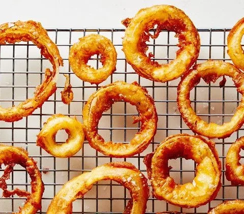 Martha Stewart beer-battered onion rings fried golden brown and cooling on a wire rack with flaky sea salt