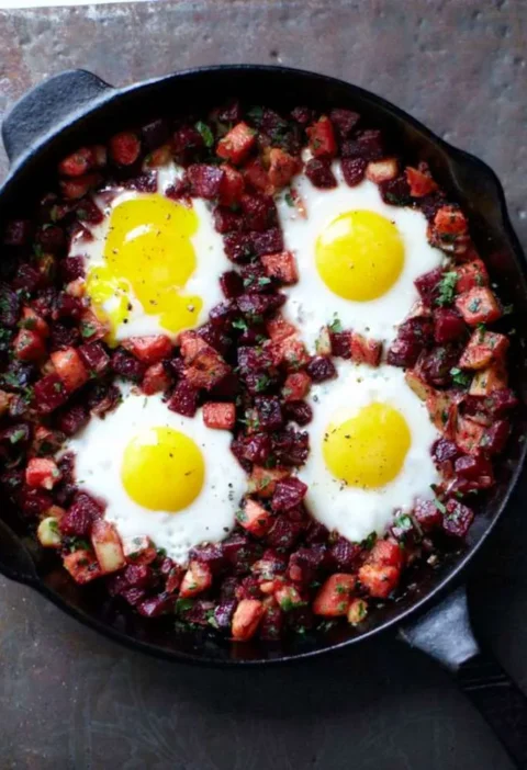 Martha Stewart beet hash with eggs in a cast iron skillet, four sunny eggs set in diced beets and potatoes