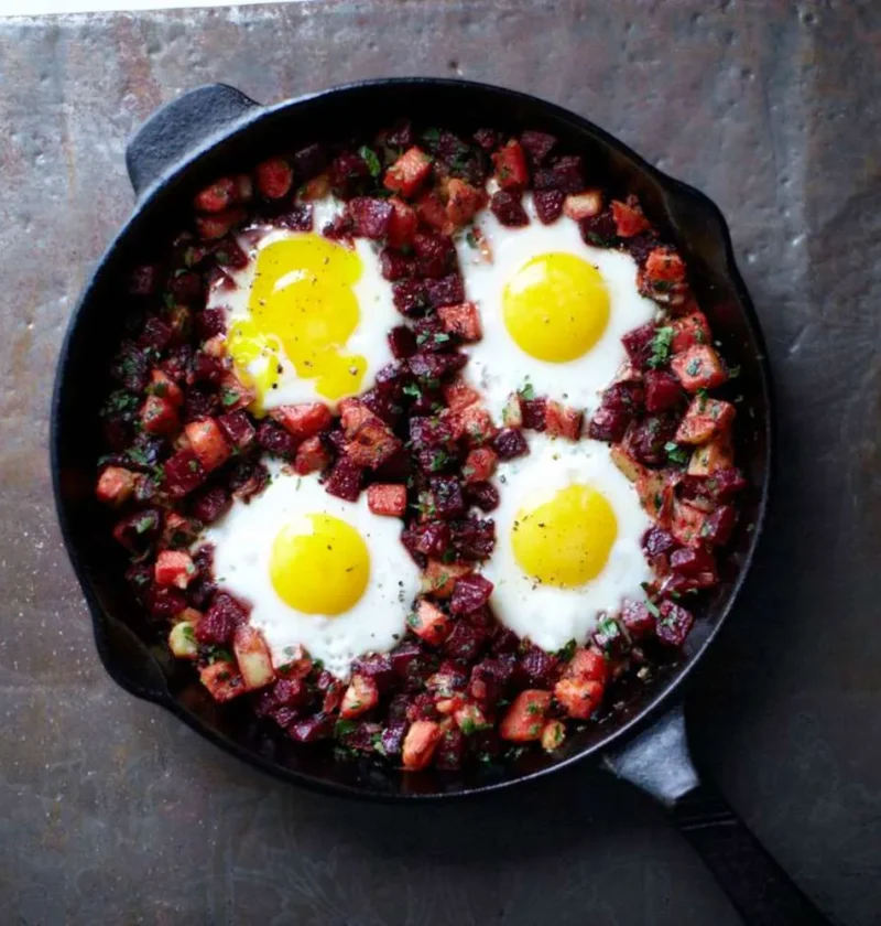 Martha Stewart beet hash with eggs in a cast iron skillet, four sunny eggs set in diced beets and potatoes