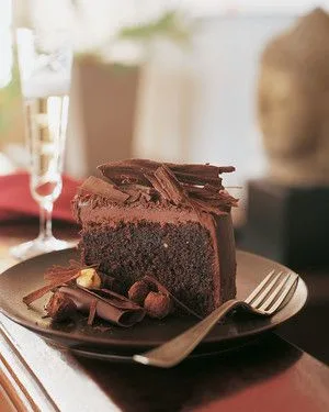 Slice of Martha Stewart Belgian chocolate birthday cake with chocolate ganache, chocolate curls and hazelnuts on a dark plate