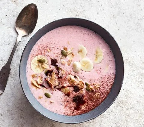 Berry-Banana Kefir Bowl with pink strawberry base topped with banana slices, granola, pumpkin seeds and cocoa powder in a gray bowl