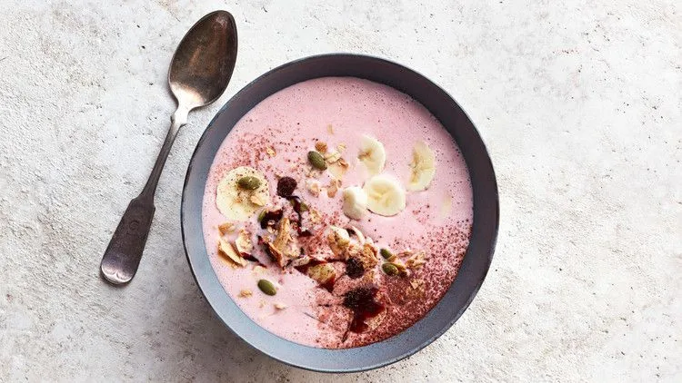 Berry-Banana Kefir Bowl with pink strawberry base topped with banana slices, granola, pumpkin seeds and cocoa powder in a gray bowl