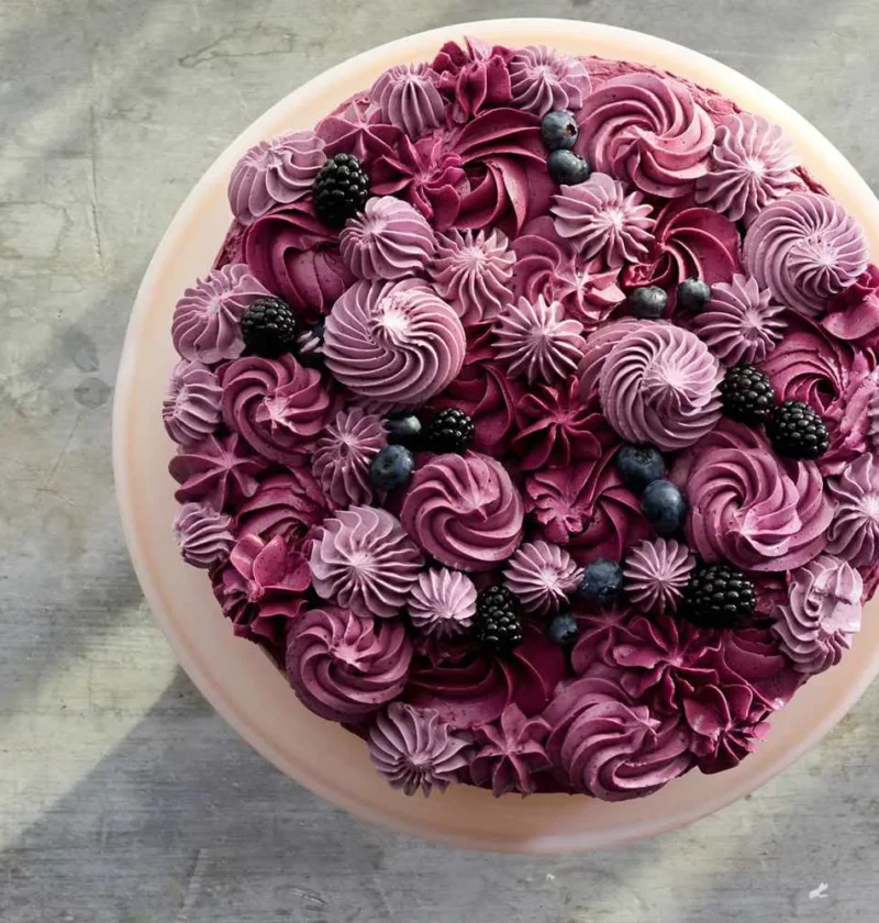 Martha Stewart berry layer cake topped with burgundy buttercream swirls, rosettes and fresh blackberries and blueberries