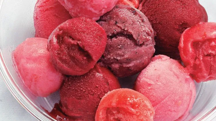Scoops of pink, red and dark purple Martha Stewart berry sorbet piled in a clear glass bowl