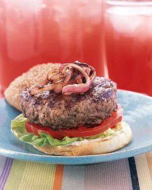 Martha Stewart best beef burger topped with grilled red onions, tomato slices and lettuce on a toasted bun
