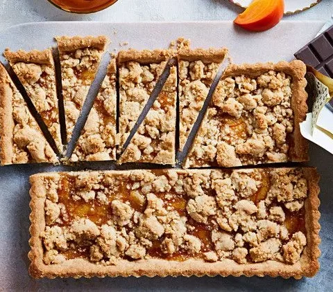 Martha Stewart big almond-orange-ginger cookie baked in a tart pan with crumb topping, cut into slices beside dark chocolate and persimmon