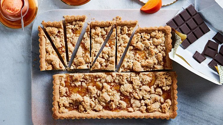 Martha Stewart big almond-orange-ginger cookie baked in a tart pan with crumb topping, cut into slices beside dark chocolate and persimmon