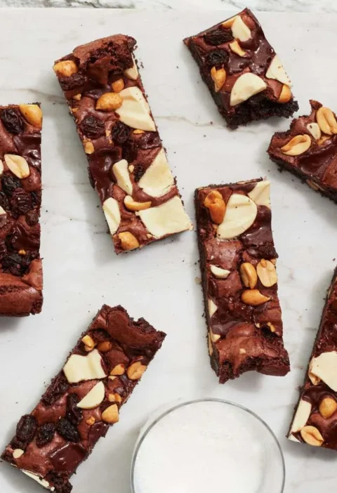 Martha Stewart big-batch triple-chocolate brownie bars topped with peanuts and white chocolate on a marble board with glasses of milk