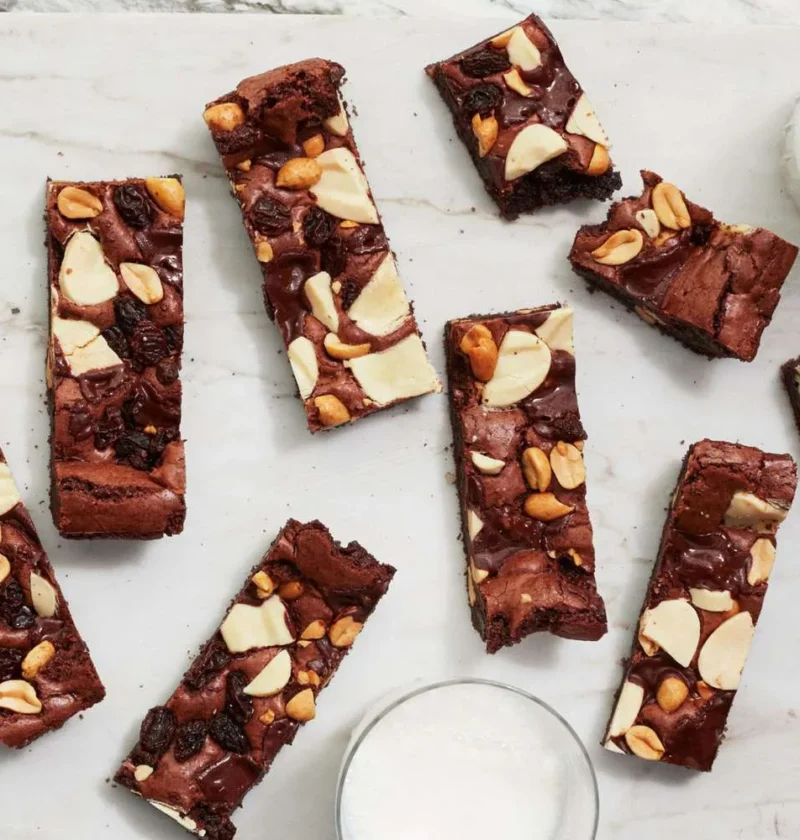 Martha Stewart big-batch triple-chocolate brownie bars topped with peanuts and white chocolate on a marble board with glasses of milk