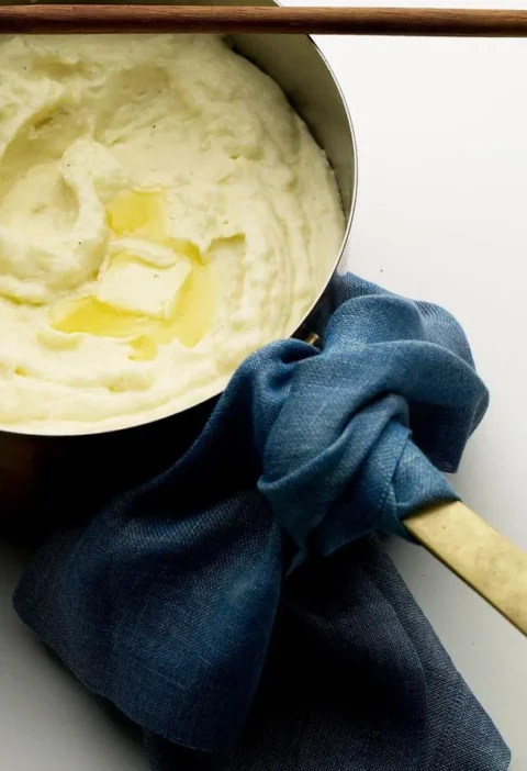 Martha Stewart Big Martha's mashed potatoes with cream cheese in a saucepan topped with melting butter and a wooden spoon