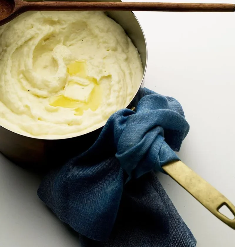 Martha Stewart Big Martha's mashed potatoes with cream cheese in a saucepan topped with melting butter and a wooden spoon