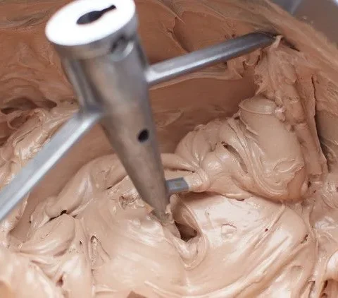 Martha Stewart Billy's chocolate buttercream frosting being mixed with a paddle attachment in a stand mixer bowl