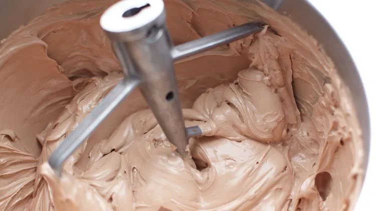 Martha Stewart Billy's chocolate buttercream frosting being mixed with a paddle attachment in a stand mixer bowl