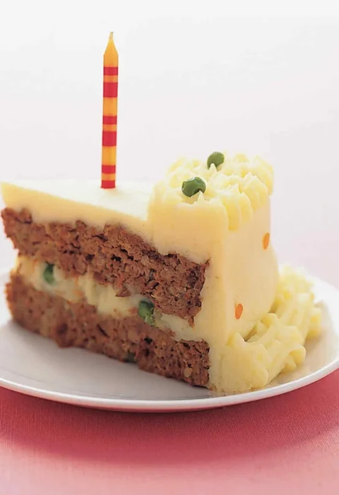 Slice of Martha Stewart birthday meatloaf cake with mashed potato frosting, green peas and a striped candle on a white plate