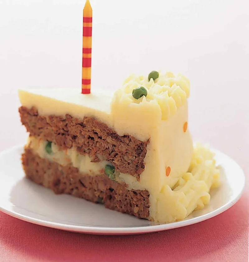 Slice of Martha Stewart birthday meatloaf cake with mashed potato frosting, green peas and a striped candle on a white plate