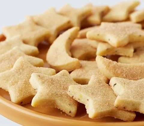 Martha Stewart biscochitos cut into stars and moons dusted with cinnamon sugar on an orange cake stand
