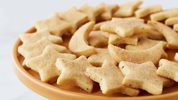 Martha Stewart biscochitos cut into stars and moons dusted with cinnamon sugar on an orange cake stand