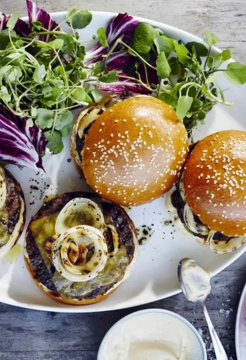 Martha Stewart bistro burgers with melted cheddar, charred onion rings and brioche buns served with watercress, radicchio, cornichons and sliced tomatoes