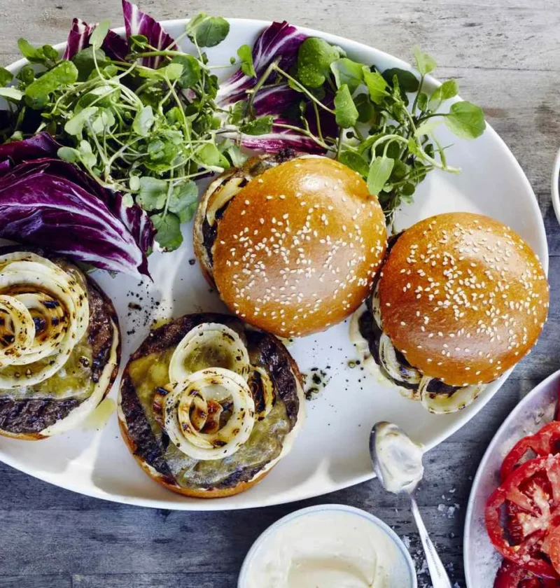Martha Stewart bistro burgers with melted cheddar, charred onion rings and brioche buns served with watercress, radicchio, cornichons and sliced tomatoes