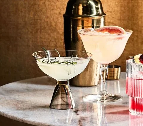 Martha Stewart Bitter Bee cocktail in a ribbed glass over ice with a grapefruit wedge garnish on a marble table