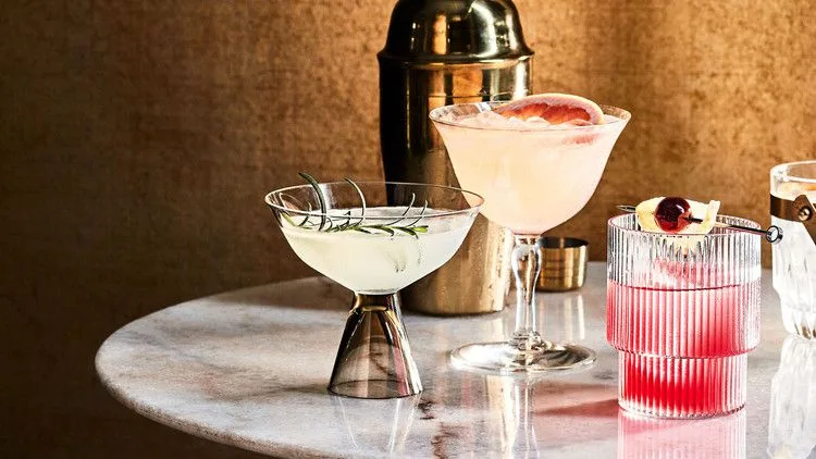 Martha Stewart Bitter Bee cocktail in a ribbed glass over ice with a grapefruit wedge garnish on a marble table