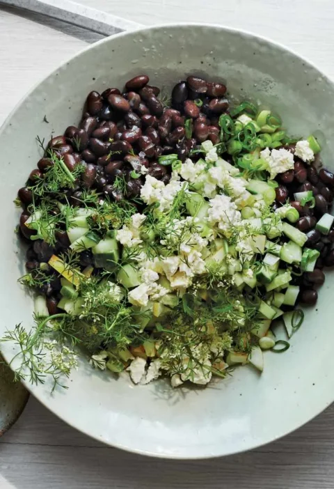 Martha Stewart black bean, cucumber, and feta salad topped with crumbled feta, diced cucumber and fresh herbs in a pale green bowl with lime halves