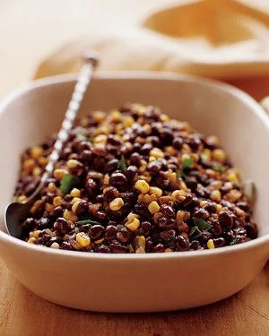 Martha Stewart black beans and corn served in a white bowl with a spoon, topped with fresh parsley