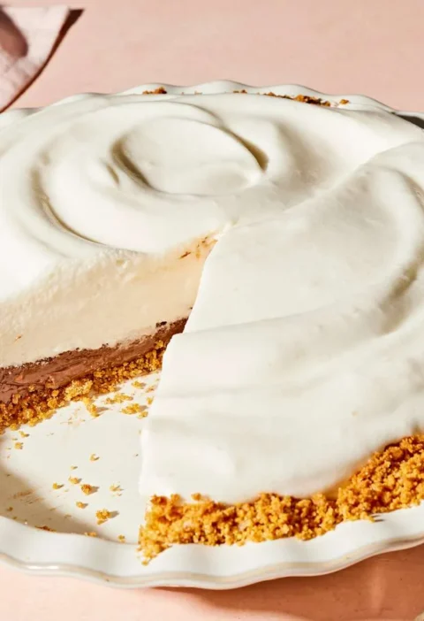 Martha Stewart black-bottom pie with a slice cut out, showing a chocolate layer under swirled white meringue in a graham cracker crust