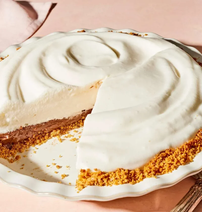 Martha Stewart black-bottom pie with a slice cut out, showing a chocolate layer under swirled white meringue in a graham cracker crust