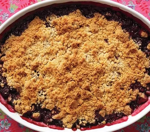 Martha Stewart blackberry crisp with a golden brown crumb topping in an oval baking dish on a floral tablecloth