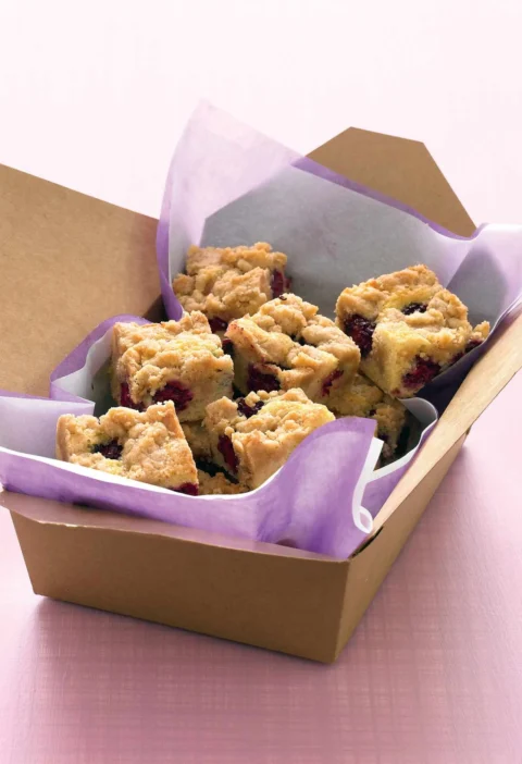 Martha Stewart blackberry crumb bars cut into squares in a brown takeout box lined with purple tissue paper