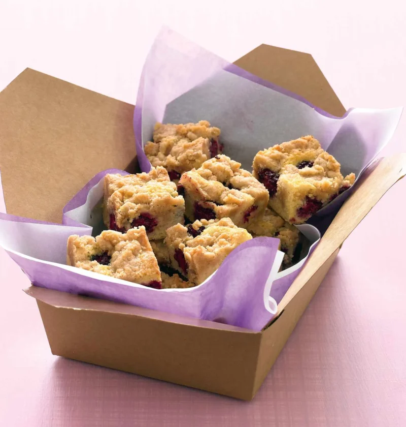 Martha Stewart blackberry crumb bars cut into squares in a brown takeout box lined with purple tissue paper