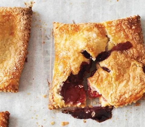 Martha Stewart blackberry-raspberry hand pies with golden flaky crust and jammy berry filling oozing from the vents on parchment paper
